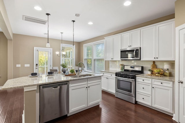 kitchen featuring sink, appliances with stainless steel finishes, white cabinetry, light stone counters, and an island with sink