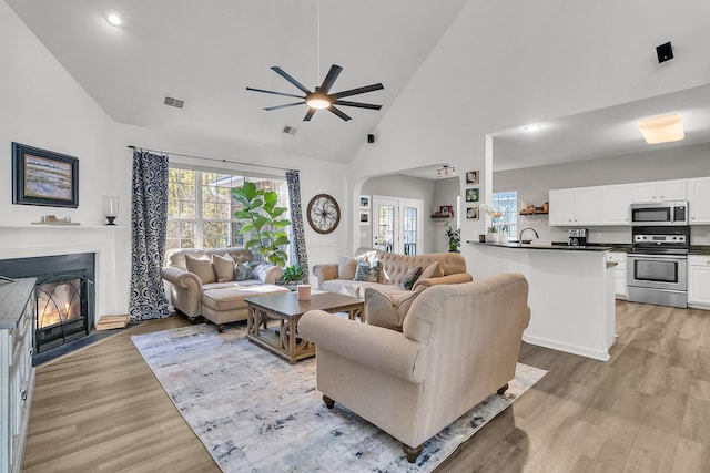 living room featuring ceiling fan, high vaulted ceiling, and light hardwood / wood-style flooring