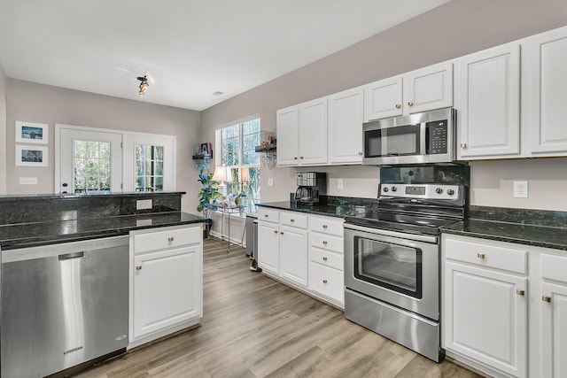 kitchen featuring white cabinetry, appliances with stainless steel finishes, a healthy amount of sunlight, and dark stone countertops