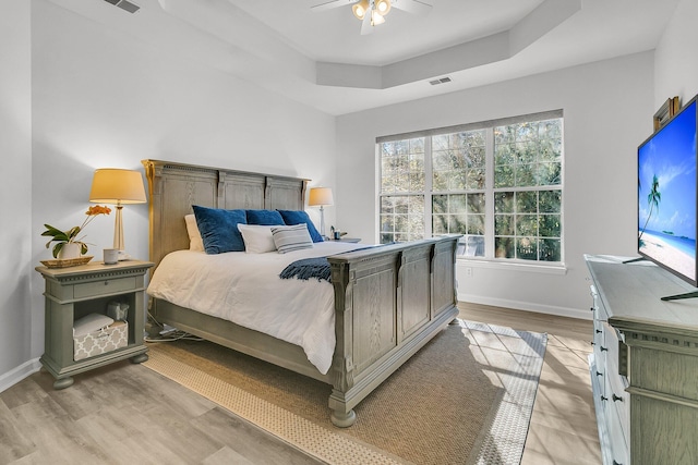 bedroom with light hardwood / wood-style flooring, a raised ceiling, and ceiling fan