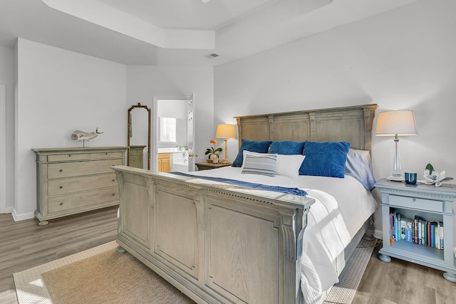 bedroom with a raised ceiling and light wood-type flooring