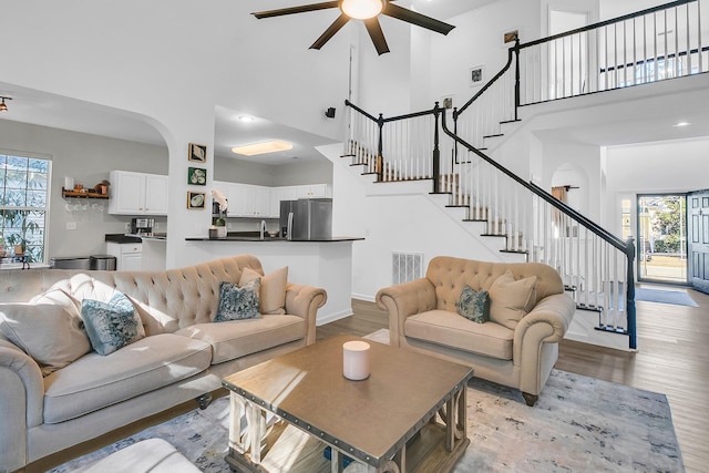 living room featuring a towering ceiling, ceiling fan, and light hardwood / wood-style flooring