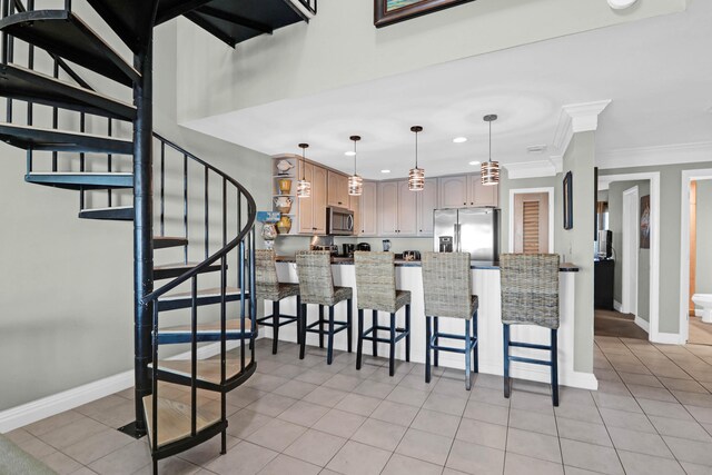 kitchen featuring hanging light fixtures, appliances with stainless steel finishes, light brown cabinetry, crown molding, and a kitchen bar