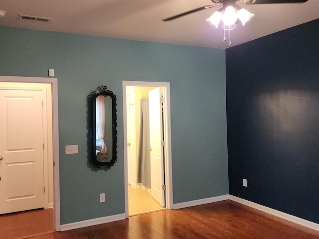 unfurnished bedroom with baseboards, visible vents, ensuite bath, ceiling fan, and wood finished floors