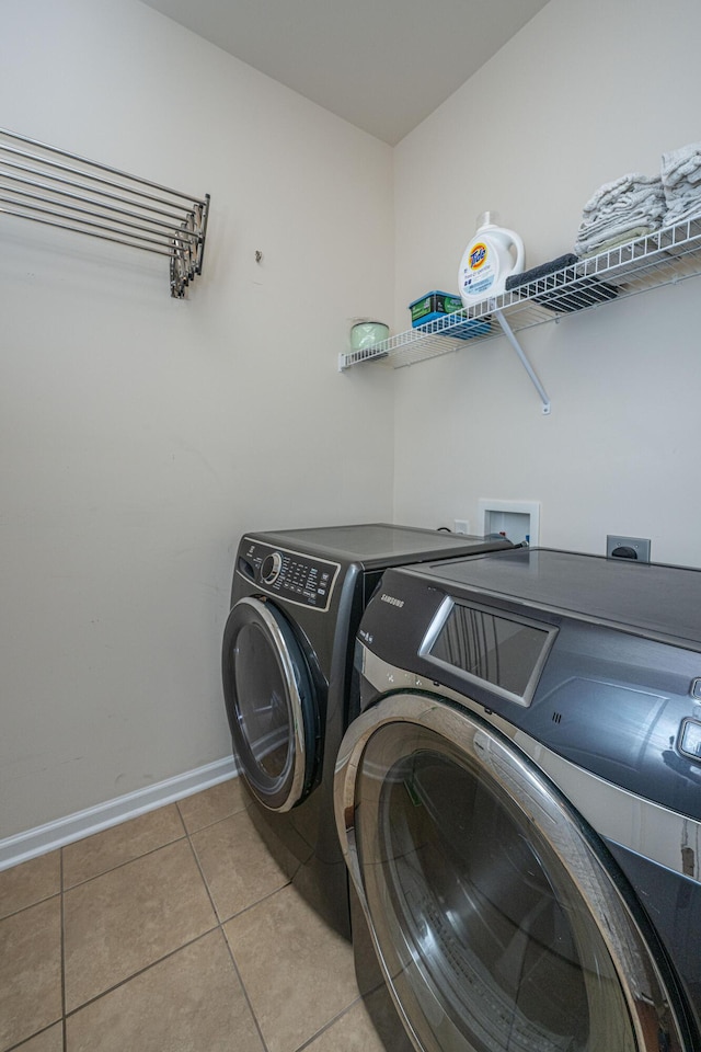 washroom with laundry area, light tile patterned flooring, baseboards, and washing machine and clothes dryer