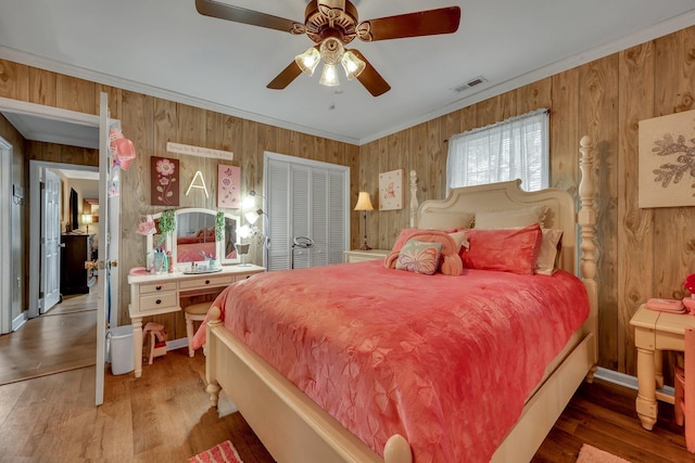 bedroom with ceiling fan, ornamental molding, wooden walls, a closet, and hardwood / wood-style flooring