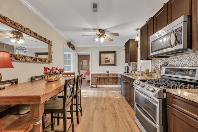 kitchen with hanging light fixtures, light wood-type flooring, ornamental molding, light stone counters, and stainless steel appliances