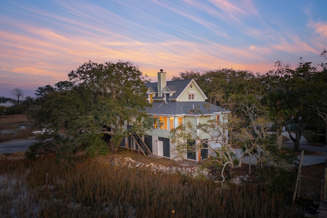 back of house at dusk featuring an attached garage, stairway, and a chimney