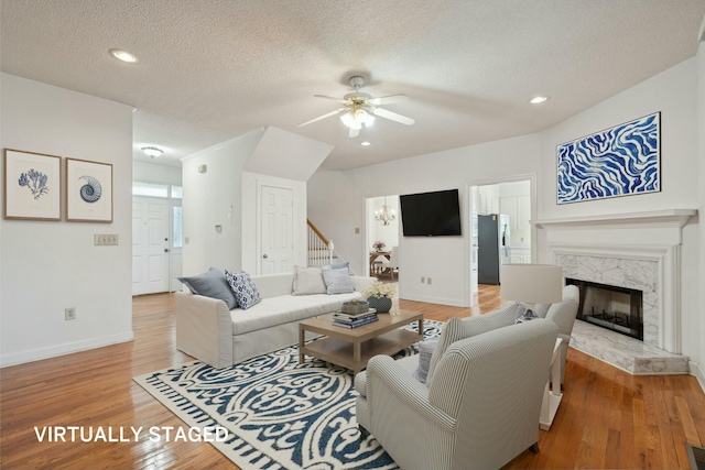 living room featuring light wood-style flooring, a premium fireplace, baseboards, and a textured ceiling