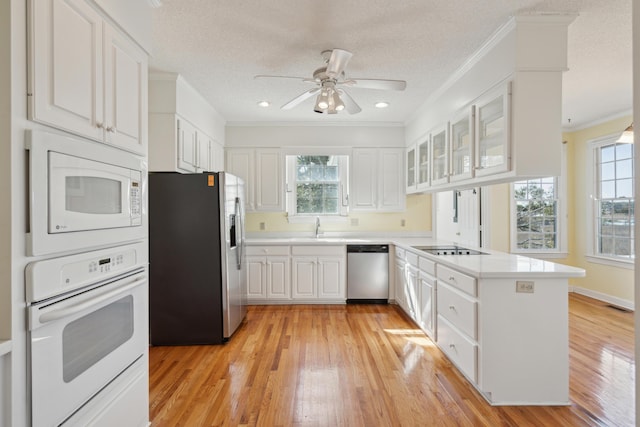 kitchen with stainless steel appliances, a peninsula, a sink, white cabinetry, and plenty of natural light