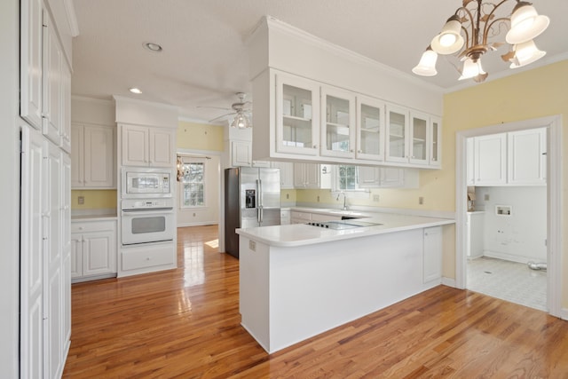 kitchen with white appliances, white cabinets, ornamental molding, a peninsula, and light wood-type flooring