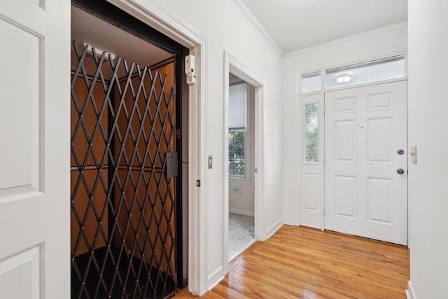 entrance foyer featuring elevator, baseboards, light wood-style floors, and crown molding