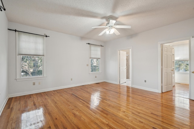 unfurnished bedroom with baseboards, ensuite bath, a textured ceiling, and light wood finished floors