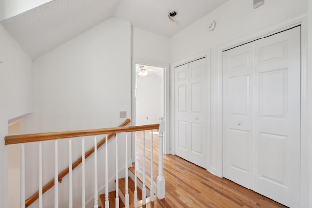 corridor with lofted ceiling, light wood finished floors, and an upstairs landing