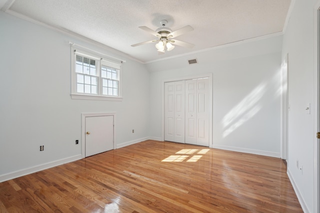 unfurnished bedroom with a textured ceiling, light wood-style flooring, visible vents, baseboards, and crown molding