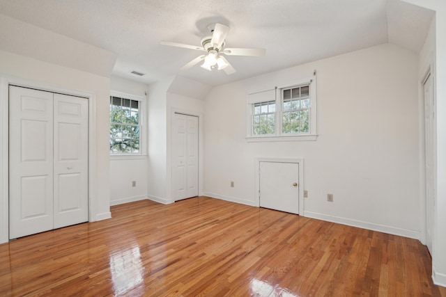 unfurnished bedroom with lofted ceiling, light wood-style floors, visible vents, and multiple closets