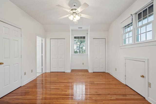 unfurnished bedroom featuring baseboards, light wood finished floors, and two closets