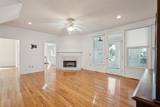 unfurnished living room with light wood-style floors, ceiling fan, a fireplace, and a textured ceiling