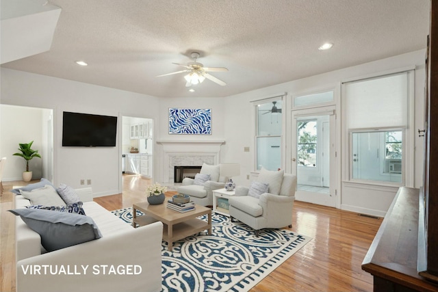 living area with light wood-style flooring, a fireplace, ceiling fan, and a textured ceiling