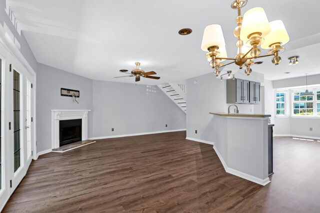 unfurnished living room featuring dark hardwood / wood-style flooring, sink, and ceiling fan with notable chandelier