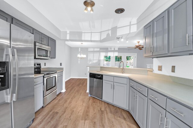 kitchen with light wood-type flooring, ceiling fan with notable chandelier, a tray ceiling, sink, and stainless steel appliances