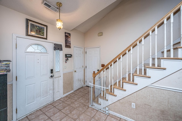 tiled entryway featuring a textured ceiling and vaulted ceiling