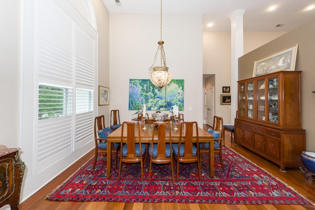 dining room with a high ceiling, decorative columns, hardwood / wood-style flooring, and a chandelier