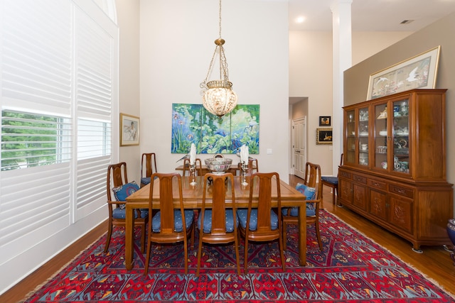 dining room with ornate columns, a notable chandelier, a towering ceiling, and hardwood / wood-style floors