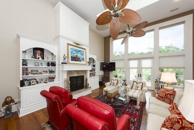 living room with built in shelves, dark wood-type flooring, ceiling fan, and a high ceiling