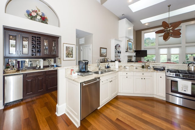 kitchen featuring a skylight, white cabinetry, dark brown cabinets, stainless steel appliances, and dark hardwood / wood-style floors