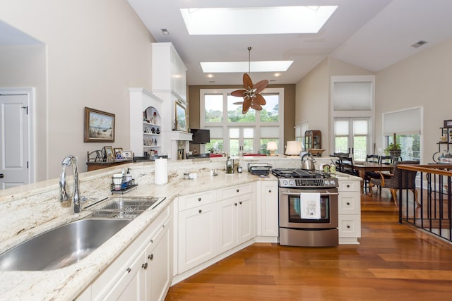 kitchen featuring a skylight, ceiling fan, sink, stainless steel range with gas cooktop, and hardwood / wood-style flooring