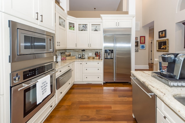 kitchen with built in appliances, backsplash, light stone counters, dark wood-type flooring, and white cabinetry