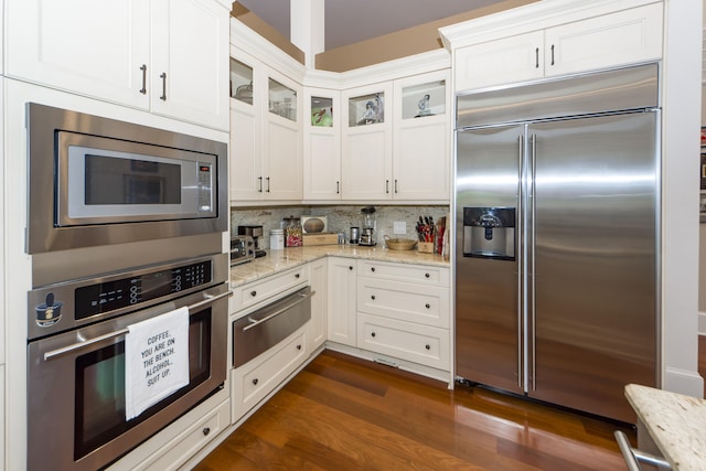 kitchen featuring built in appliances, dark wood-type flooring, tasteful backsplash, and light stone countertops