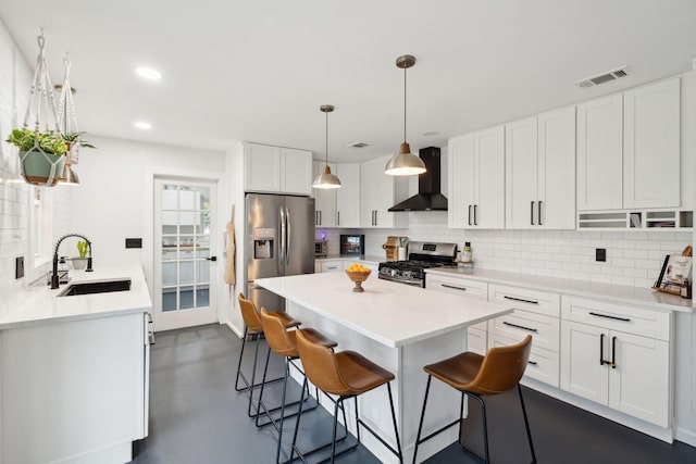 kitchen with pendant lighting, wall chimney range hood, white cabinetry, appliances with stainless steel finishes, and sink