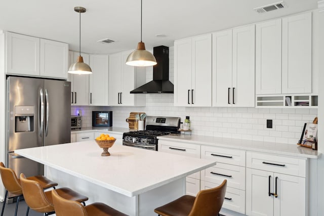 kitchen with white cabinetry, a kitchen bar, hanging light fixtures, wall chimney range hood, and appliances with stainless steel finishes