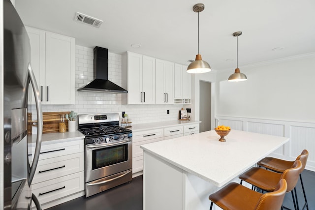 kitchen featuring white cabinets, wall chimney range hood, hanging light fixtures, and appliances with stainless steel finishes