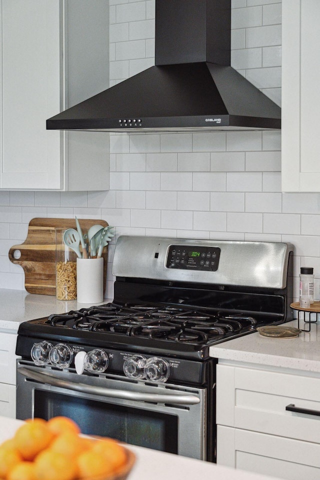 kitchen with white cabinetry, wall chimney range hood, gas stove, and tasteful backsplash