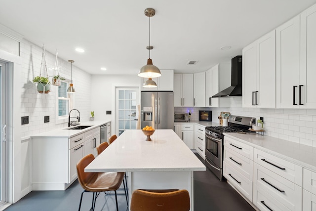 kitchen featuring appliances with stainless steel finishes, pendant lighting, wall chimney exhaust hood, white cabinets, and sink