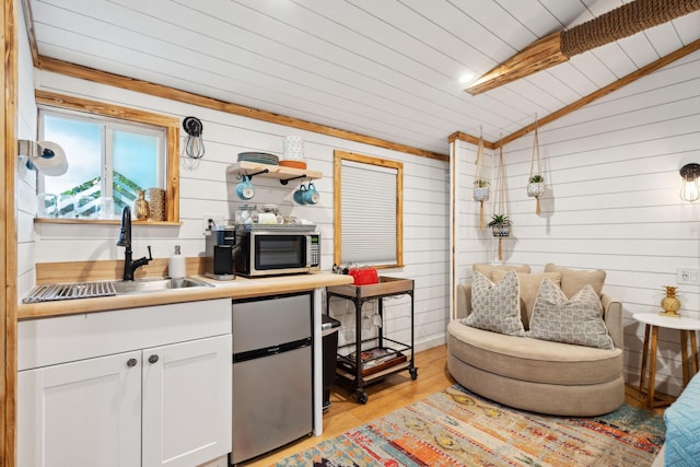 kitchen with lofted ceiling with beams, wooden walls, light hardwood / wood-style floors, white cabinets, and sink