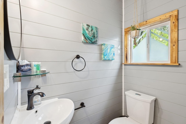 bathroom featuring sink, wooden walls, and toilet