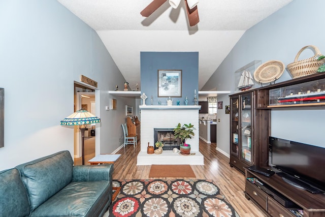 living room featuring ceiling fan, a fireplace, light hardwood / wood-style floors, and vaulted ceiling