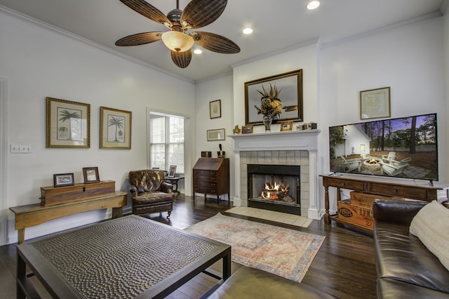 living area with crown molding, ceiling fan, dark hardwood / wood-style floors, and a tile fireplace