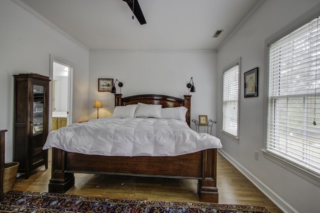 bedroom featuring connected bathroom, dark wood-type flooring, ornamental molding, and ceiling fan