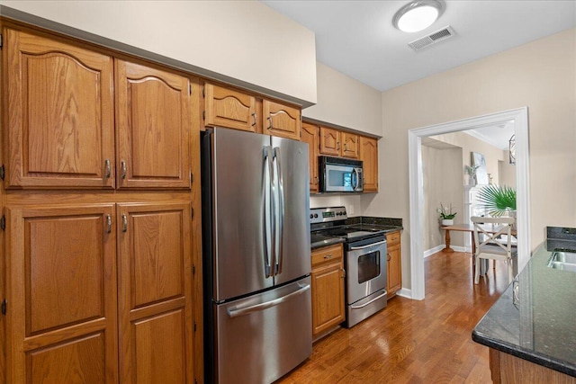 kitchen with hardwood / wood-style flooring, dark stone countertops, and appliances with stainless steel finishes