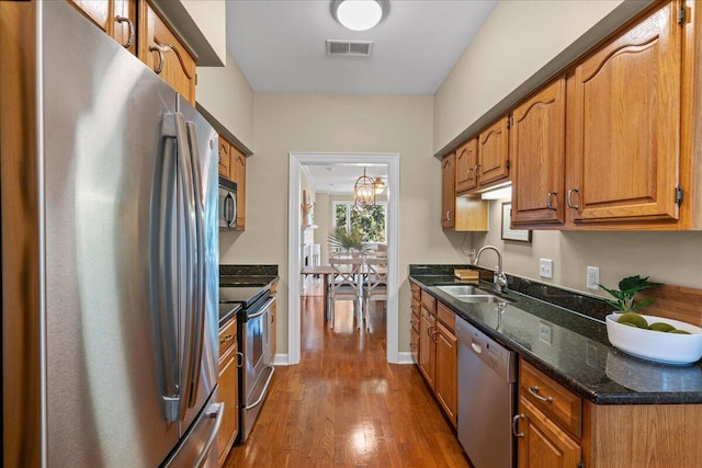 kitchen featuring sink, an inviting chandelier, dark hardwood / wood-style flooring, dark stone countertops, and appliances with stainless steel finishes