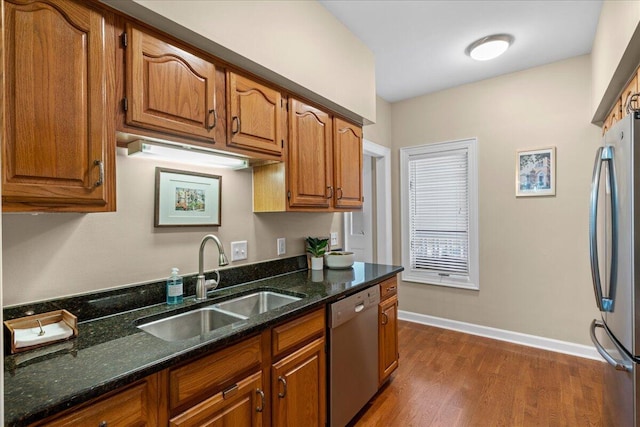 kitchen featuring appliances with stainless steel finishes, dark hardwood / wood-style flooring, dark stone countertops, and sink