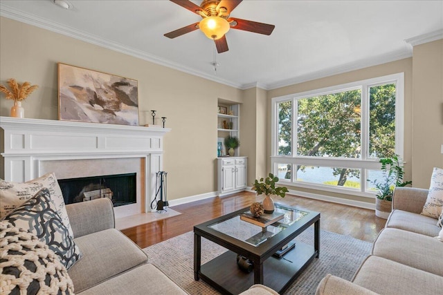 living room with built in shelves, a premium fireplace, hardwood / wood-style floors, and ornamental molding