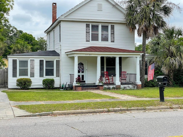 view of front facade featuring covered porch, a chimney, and a front yard