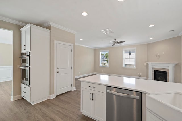 kitchen with appliances with stainless steel finishes, light hardwood / wood-style flooring, crown molding, white cabinets, and ceiling fan