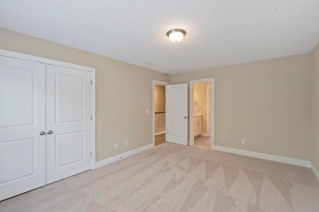 unfurnished bedroom with baseboards, a closet, connected bathroom, and light colored carpet